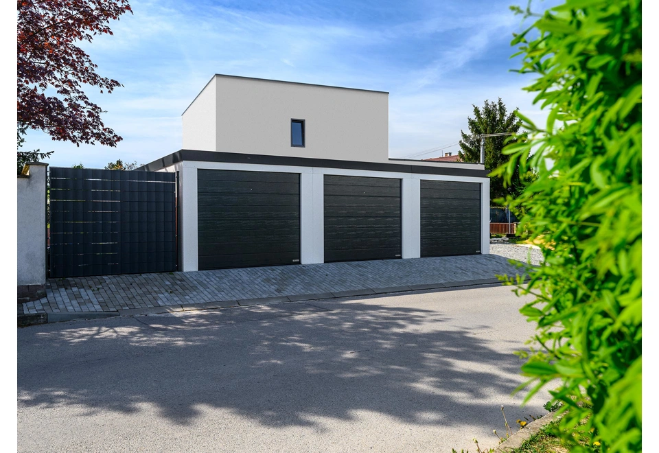 Řadová montovaná garáž pro tři auta s bílou omítkou a třemi sekčními garážovými vraty.