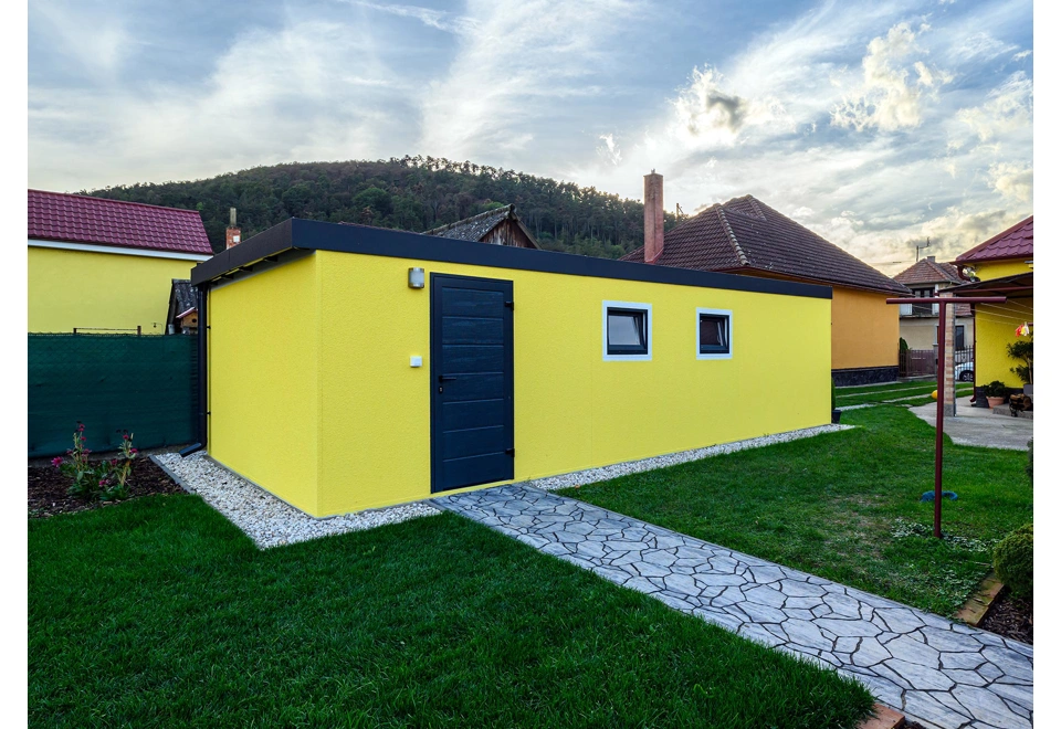 Montovaná garáž 4 x 7 m se žlutou omítkou, zateplenými dveřmi, dvěma okny a atikou v antracitové barvě.