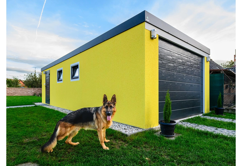 Montovaná garáž 4 x 7 m se žlutou omítkou, zateplenými dveřmi, dvěma okny a atikou v antracitové barvě.