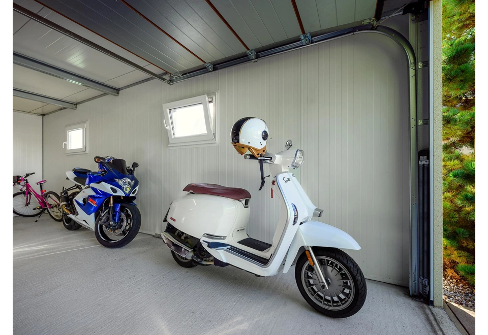 Interiér montované garáže 4,5 x 7 m s bílými stěnami, dvěma okny a sekčními garážovými vraty.