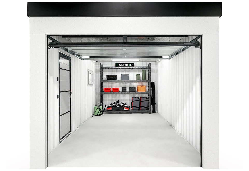 Interiér montované garáže 3 x 6 m s kovovým regálem, bílými stěnami, oknem a zateplenými dveřmi.