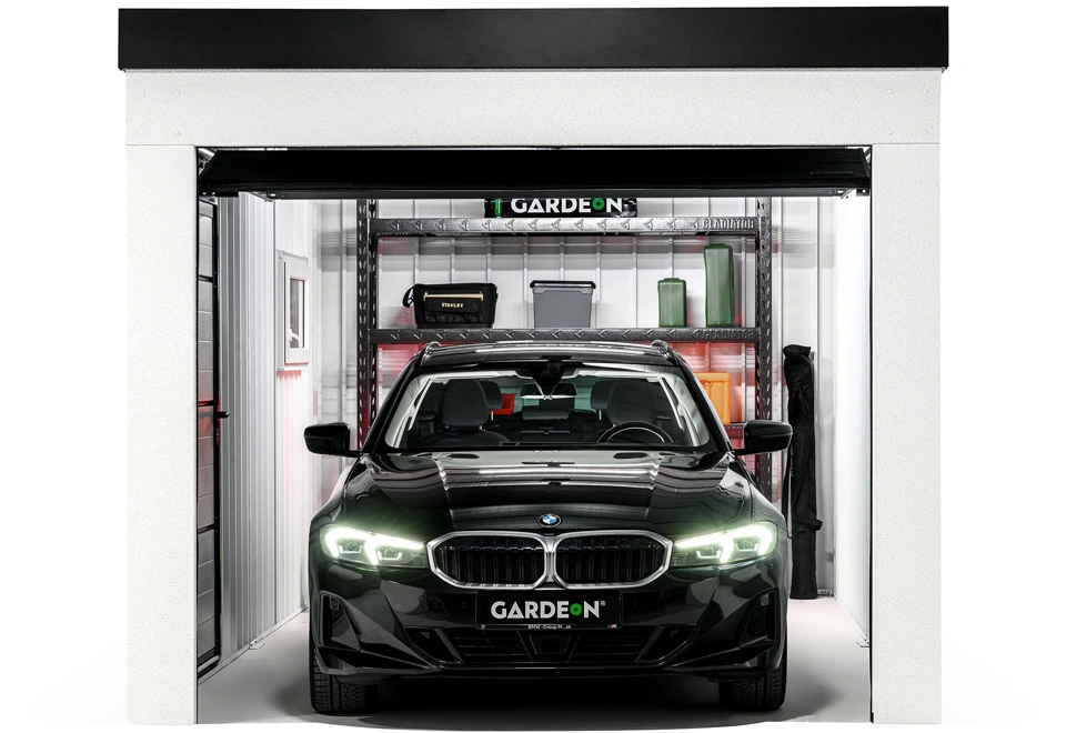 Interiér montované garáže 3 x 6 m s kovovým regálem, bílými stěnami, oknem a zateplenými dveřmi.