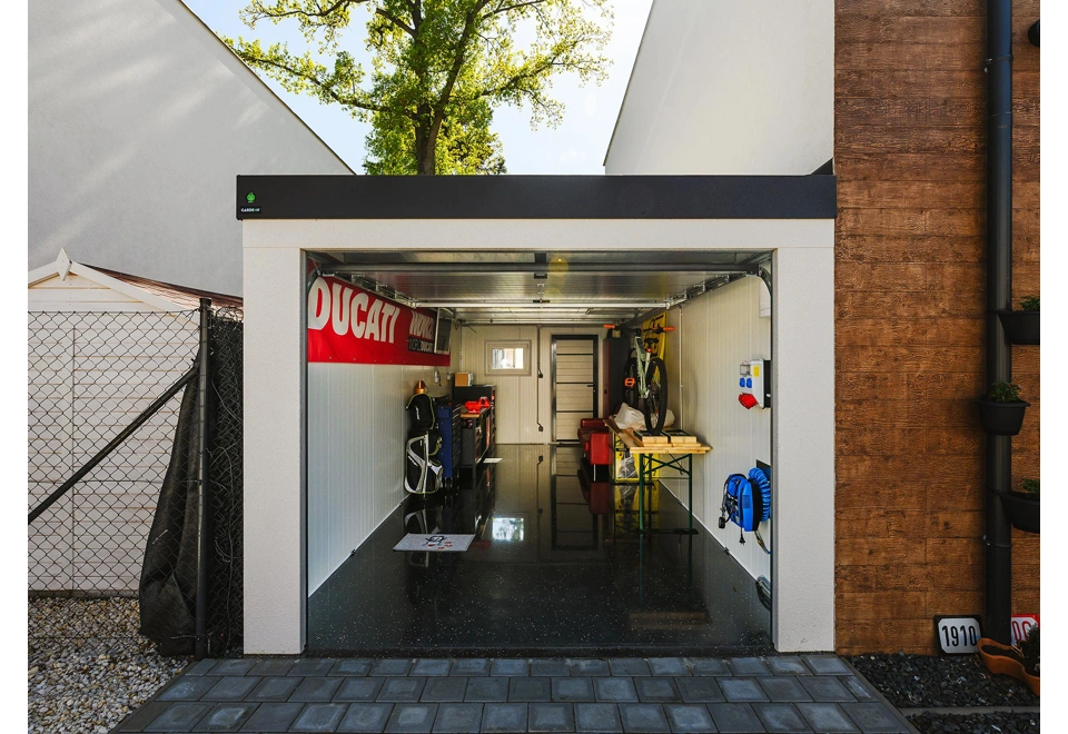 Vybavená montovaná garáž 3 x 7 m s bílými stěnami, oknem a zateplenými dveřmi.