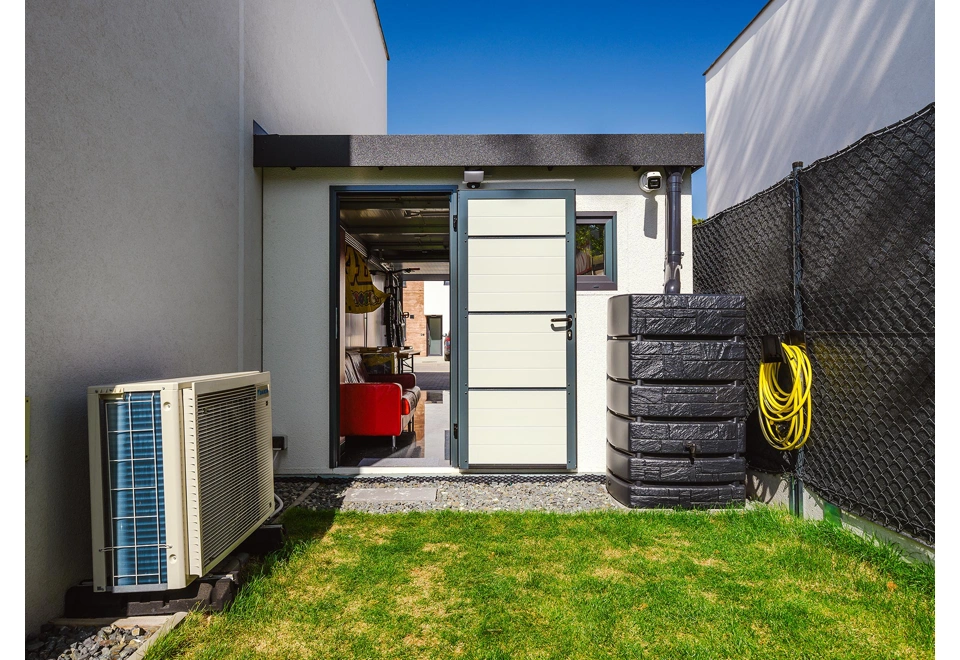 Zateplené jednokřídlé dveře montované garáže 3 x 7 m s oknem, bílou omítkou a černými doplňky včetně okapu.