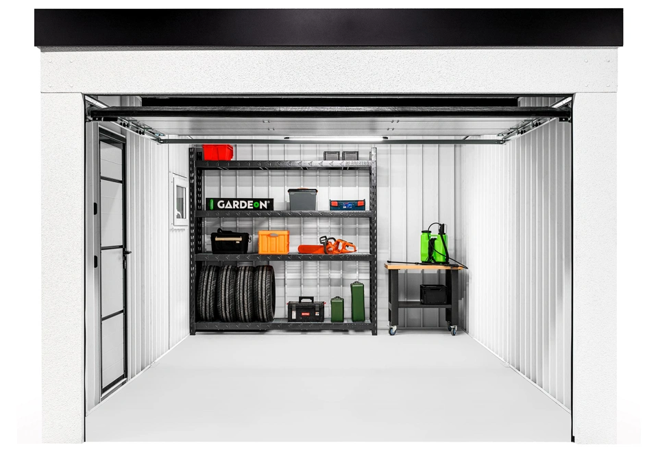 Interiér montované garáže 3,5 x 6 m s oknem, zateplenými jednokřídlými dveřmi, bílými stěnami, regálem a dílenským stolem.