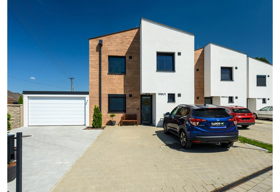 Montovaná garáž 5,8 x 5 m s bílými sekčními vraty, bílou omítkou a atikou v černé barvě.