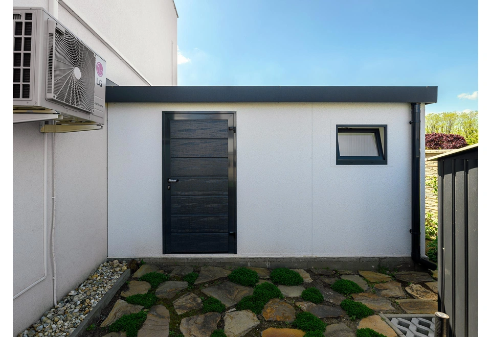 Montovaná garáž 5,8 x 5 m s bílou omítkou, oknem, zateplenými dveřmi a atikou v černé barvě s okapem.