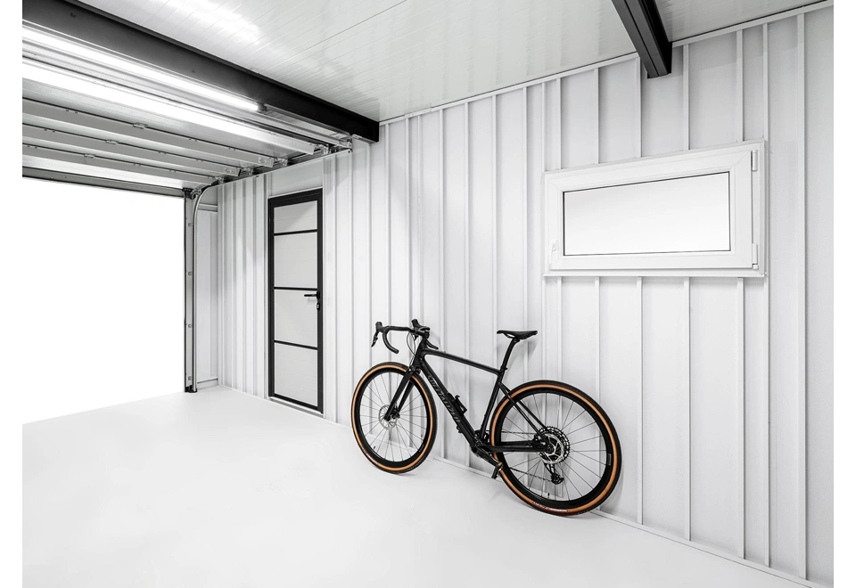 Interiér montované garáže 5,8 x 5 m s bílými stěnami, oknem a jednokřídlými zateplenými dveřmi.