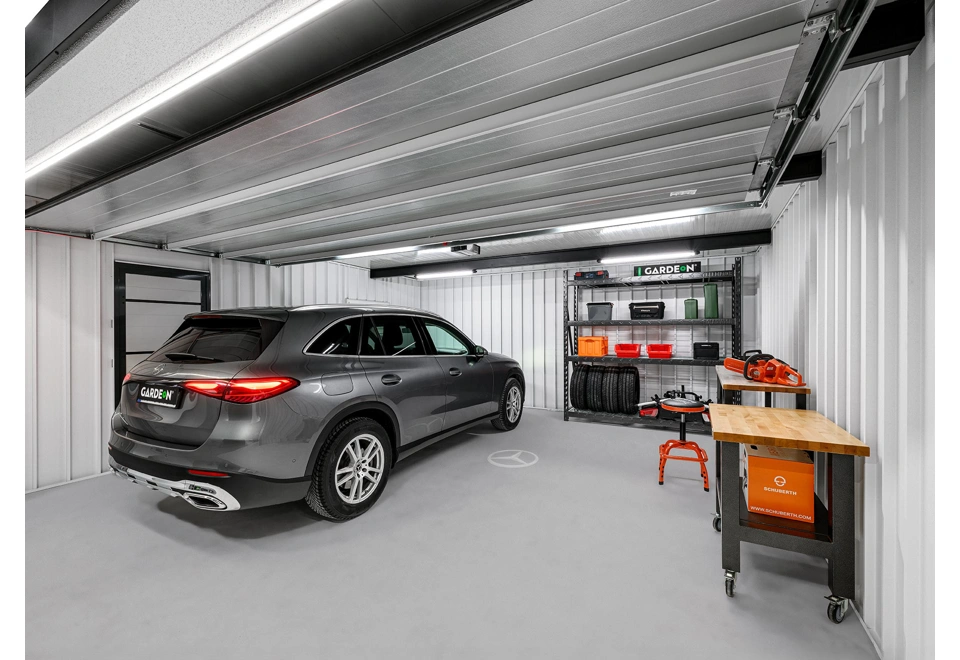 Interiér montované garáže 5,8 x 5 m s bílými stěnami, zateplenými dveřmi, regálem a dílenskými stoly.