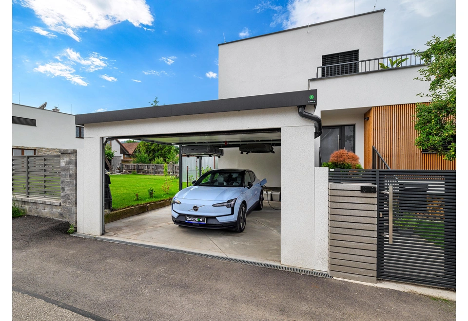 Otevřená garážová vrata přístřešku na auto 5 x 6 m s bílou omítkou, černou atikou a okapem.