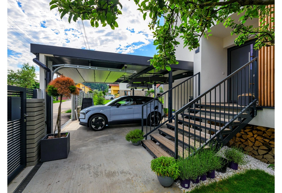 Polouzavřený přístřešek na auto 5 x 6 m s garážovými vraty, atika a okap v černé barvě.