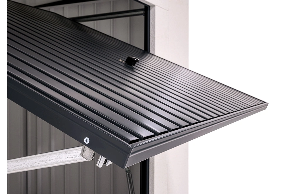 Detail výklopných garážových vrat v antracitové barvě zahradního domku 3,5 x 2 m s bílou omítkou.