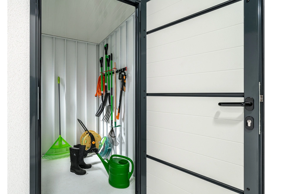 Zateplené dveře zahradního domku 3 x 2 m a interiér s držákem nářadí, bílé stěny a zateplená střecha.
