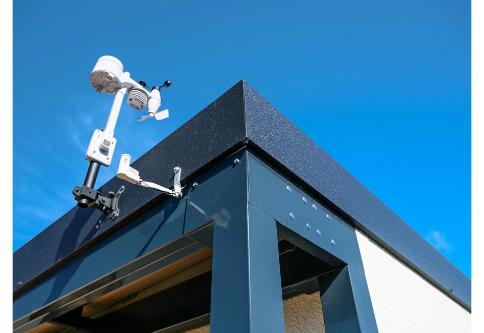 Detail rohu montovaného zahradního domku 4 x 3 m s přístřeškem, bílou omítkou a antracitovou atikou.