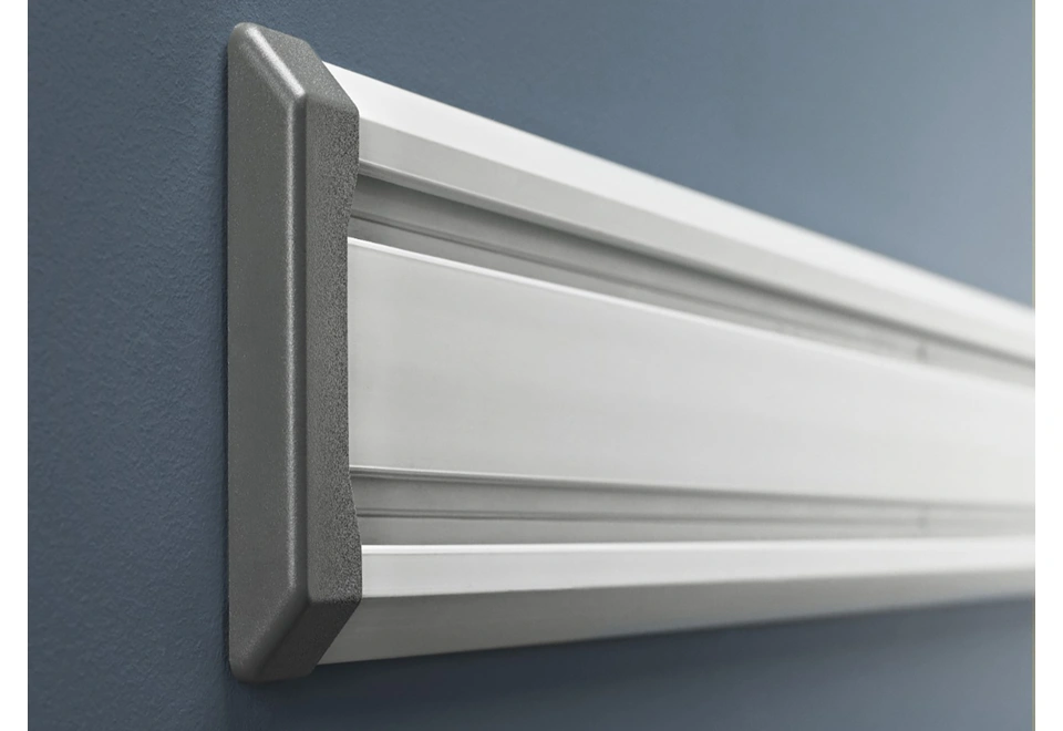 Detail černé krytky na nástěnné hliníkové kolejnice umístěné na zdi.