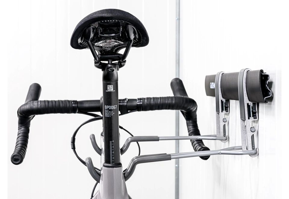 Uchycení cyklistického kola na závěsném systému na bílé stěně zahradního domku GARDEON®.